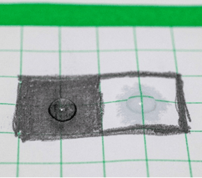At 30 seconds, a drop of water sitting on top of a black graphite box and a second smaller drop of water sitting on top of a white paper box with a growing ring of water around it that has soaked into the paper.